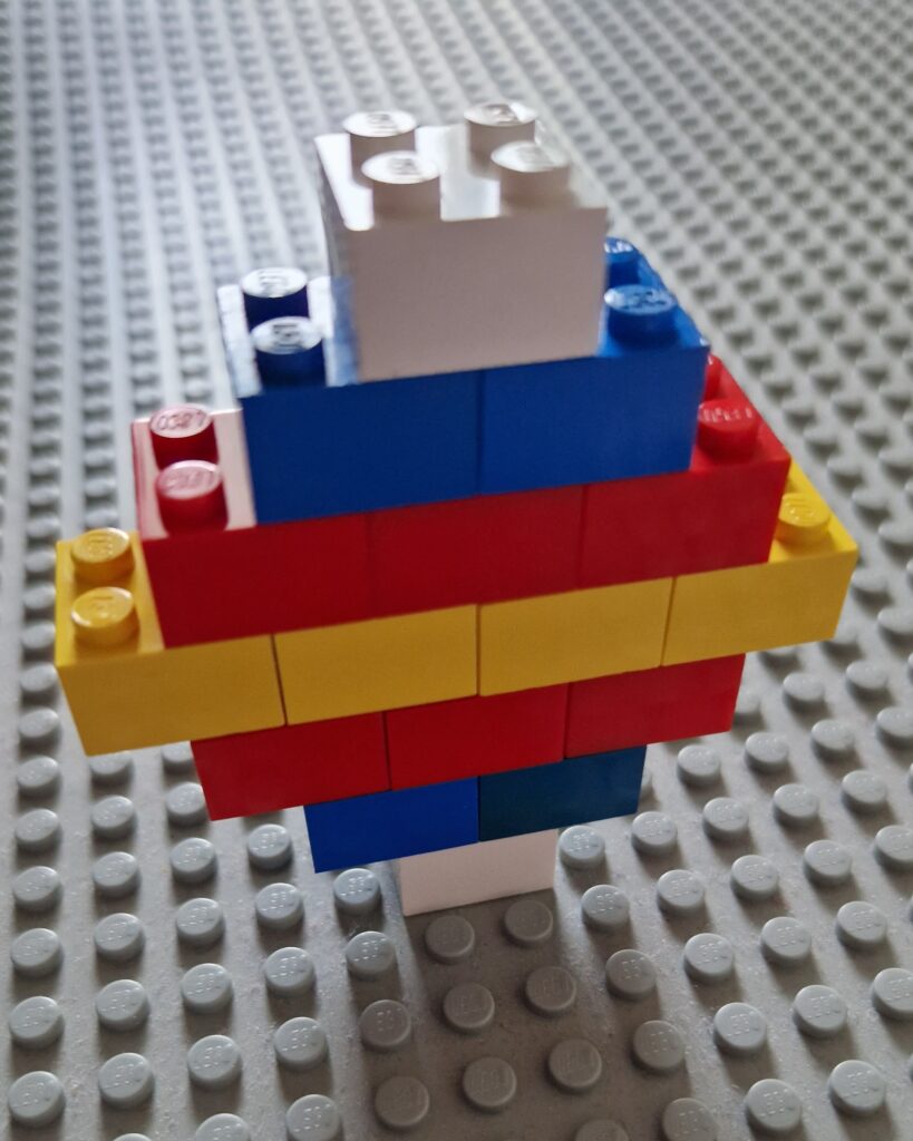 A lozenge shape made out of 2 by 2 lego bricks, standing up on a grey baseboard. Rows from bottom to top: 1 white, 2 blue, 3 red, 4 yellow, 3 red, 2 blue, 1 white